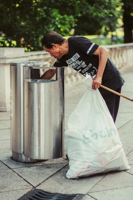 A small blue pickup truck with visible rust and wear parked on the side of a street, loaded with various types and sizes of waste materials including cardboard boxes, bags, and other scattered debris,